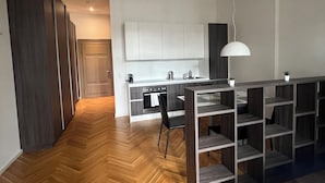 A modern kitchen with white cabinets, a built-in oven, and a dining area with a wooden herringbone floor.