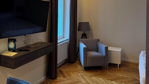 A hotel room with a flat-screen TV, a small table with a remote control, a lamp, a chair, and a bed.