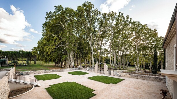 Une cour avec quatre zones de pelouse verdoyante, un mur de pierre et une clôture en métal.
