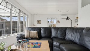 A modern living room with a black leather sectional sofa, a wooden coffee table, and a large window with a view of the outside.