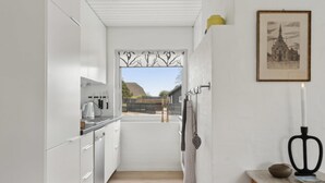 A narrow kitchen with white cabinets, a wooden countertop, and a view of a building outside.