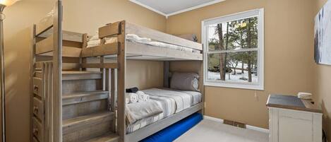 A bunk bed room with a window, a desk, and a lamp.