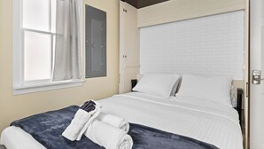 Une chambre d’hôtel avec un lit, une fenêtre avec des rideaux, une porte et un luminaire fixé au mur.