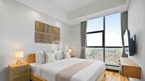 A modern hotel room with a large bed, a bedside table with a lamp, a wall-mounted TV, and a large window offering a city view. - Hanae by Kozystay - Kuningan (Jakarta)