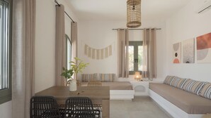 Uma sala de estar moderna com área de jantar, apresentando um sofá, uma mesa com cadeiras, um lustre e vista para o exterior.