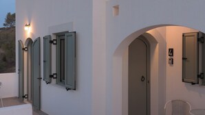 Um edifício moderno com paredes brancas, portas em arco e uma pequena área externa com uma mesa e uma cadeira.
