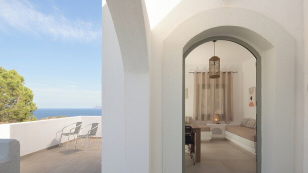Uma varanda com vista para o mar, área de estar com mesa e cadeiras, e luminária pendente.