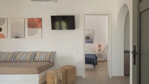 Quarto moderno e bem iluminado com sofá, obras de arte nas paredes, televisão de tela plana e cama com luminária.