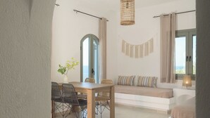Uma sala de estar ampla com uma mesa de jantar, cadeiras e um sofá. Há uma janela grande que oferece vista para o exterior.