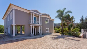 Ein zweistöckiges Haus mit Balkon, Auffahrt und umliegender Bepflanzung.
