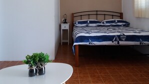 Een slaapkamer met een bed, een klein nachtkastje, een wandairconditioner, een lijst met een afbeelding en een tafeltje met een plant.
