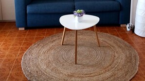 Een woonkamer met een blauwe bank, een witte salontafel en een geweven vloerkleed.