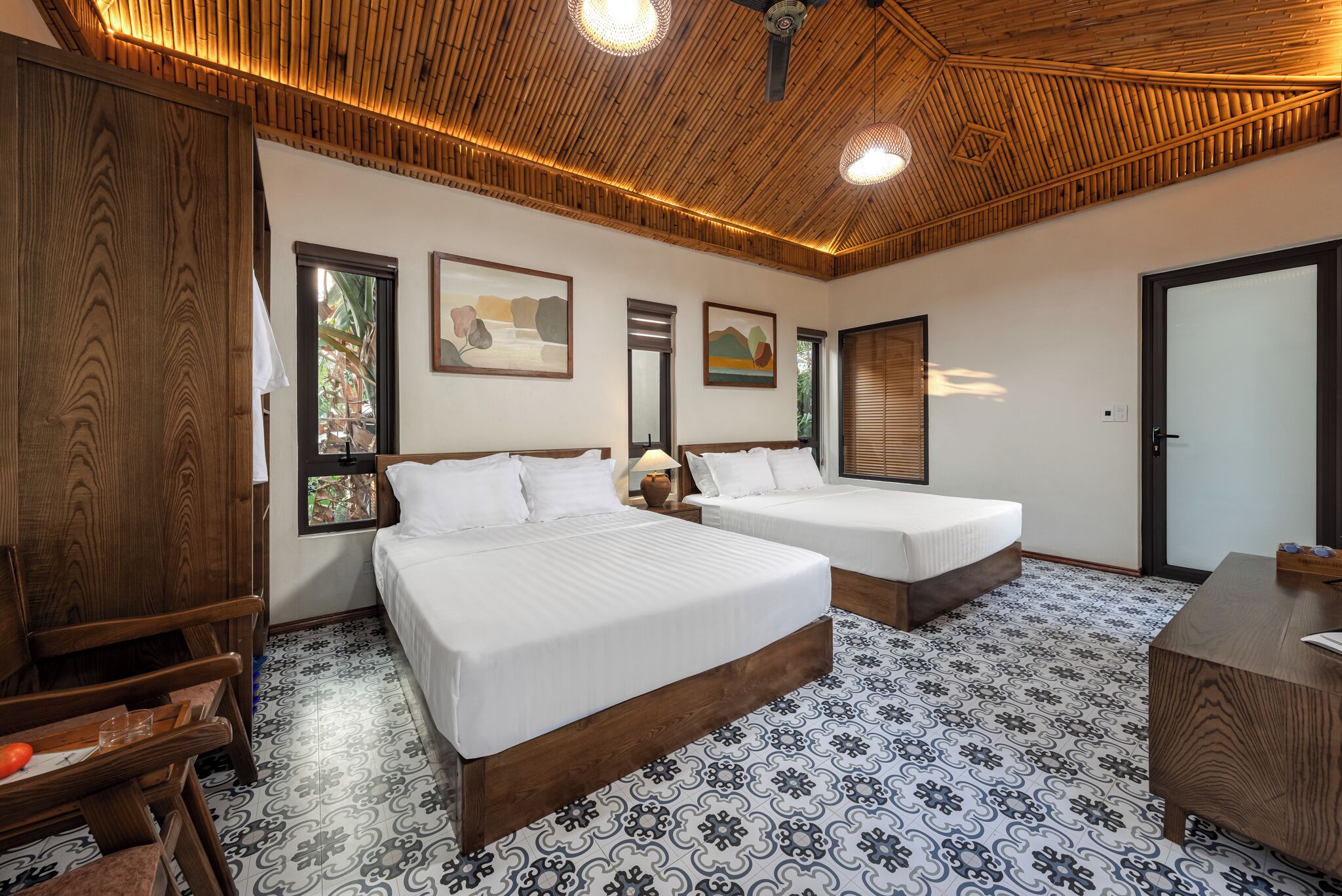 A room with two beds, wooden ceiling, patterned floor, and artwork on the walls.