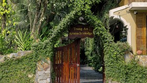 A wooden gate with a sign reading "Trang An Aroma Ecolodge" leading to a stone pathway. - Trang An Aroma Homestay (Ninh Binh)