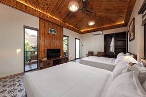 A hotel room with two beds, a television, a ceiling fan, and a large window with a view of greenery. - Trang An Aroma Homestay (Hoa Lu)