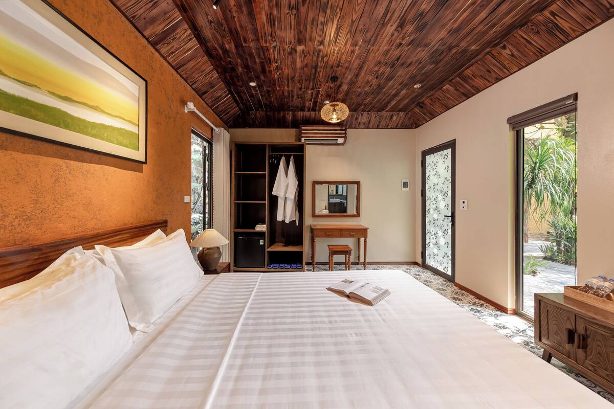Un'ampia camera da letto con un letto grande, soffitto in legno e vista sull'esterno tramite una porta scorrevole.