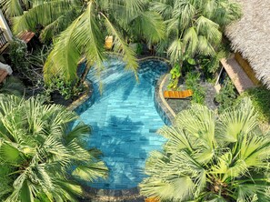 Una piscina amplia y cristalina rodeada de exuberante vegetación tropical, con palmeras y otra vegetación.