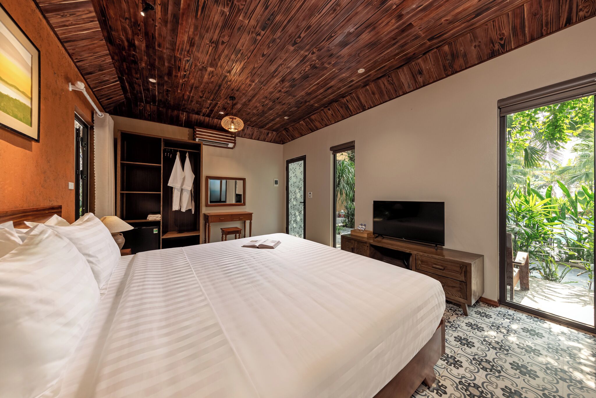 Une chambre avec un grand lit, un plafond en bois, une télévision, une armoire et une vue sur la verdure.