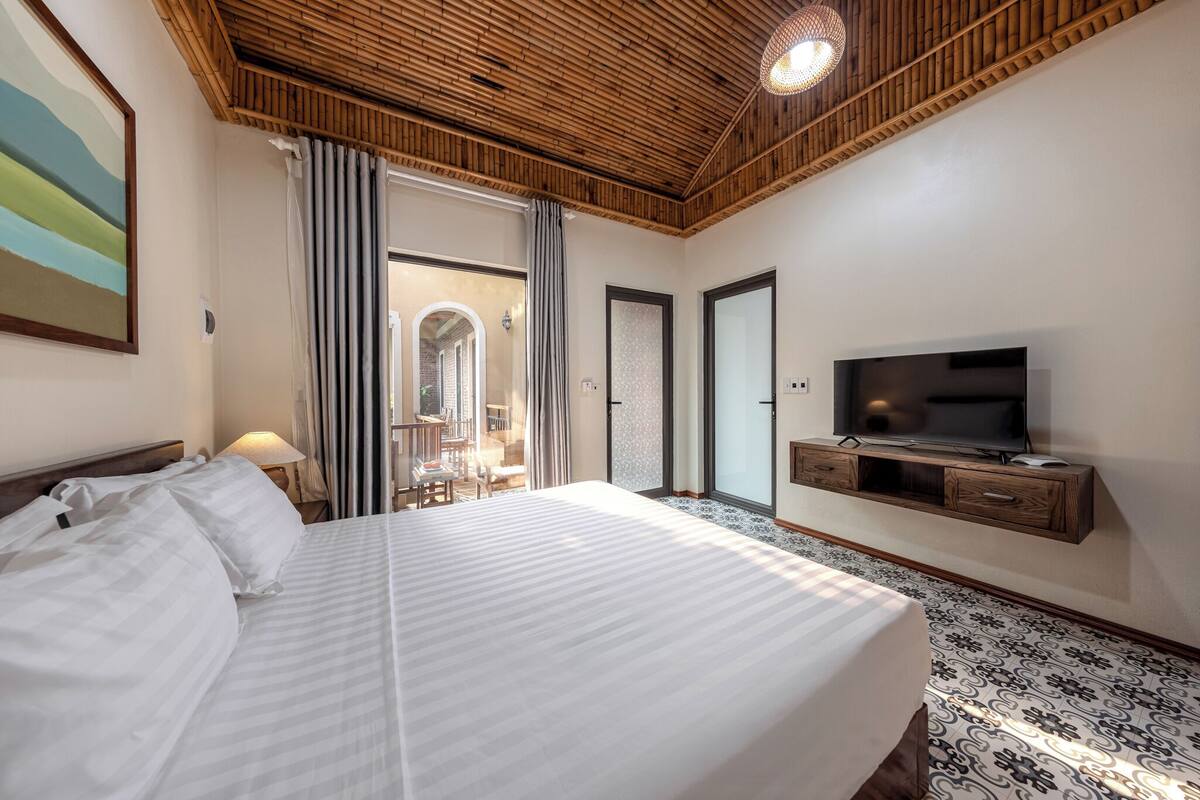 Camera d'albergo con un letto grande, una TV su una mensola di legno e vista all'esterno tramite una porta.