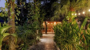 A stone pathway leading to a wooden structure with hanging lights, surrounded by lush tropical plants. - Trang An Aroma Homestay (Ninh Binh)