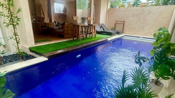 Una piscina con superficie d'acqua cristallina e azzurra, circondata da piante in vaso e un patio con mobili da esterno.