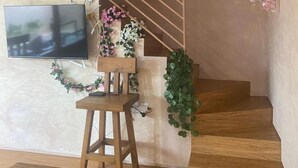 Una scala con gradini in legno e una ringhiera, una panca di legno, un tavolino con un vaso di fiori e una televisione a schermo piatto montata a parete.