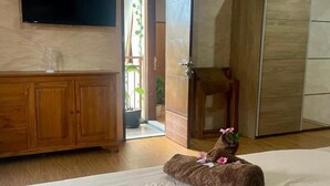 Una camera d'albergo con un letto, un armadio in legno, una televisione a muro e una porta che dà su un'altra stanza.
