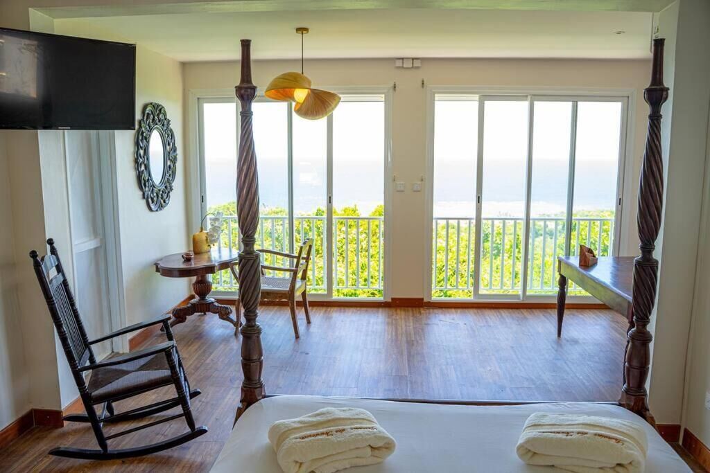 Un dormitorio con una cama grande, una mecedora, una mesita con lámpara y un balcón con vistas.