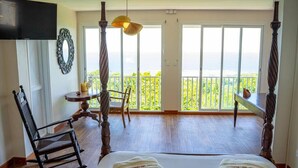 A bedroom with a large bed, a rocking chair, a small table with a lamp, and a balcony with a view.