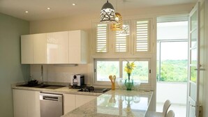 A modern kitchen with a central island, white cabinetry, and a view of greenery through the windows.