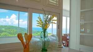 A kitchen with a view of the ocean, a green vase with yellow flowers, and wooden utensils.
