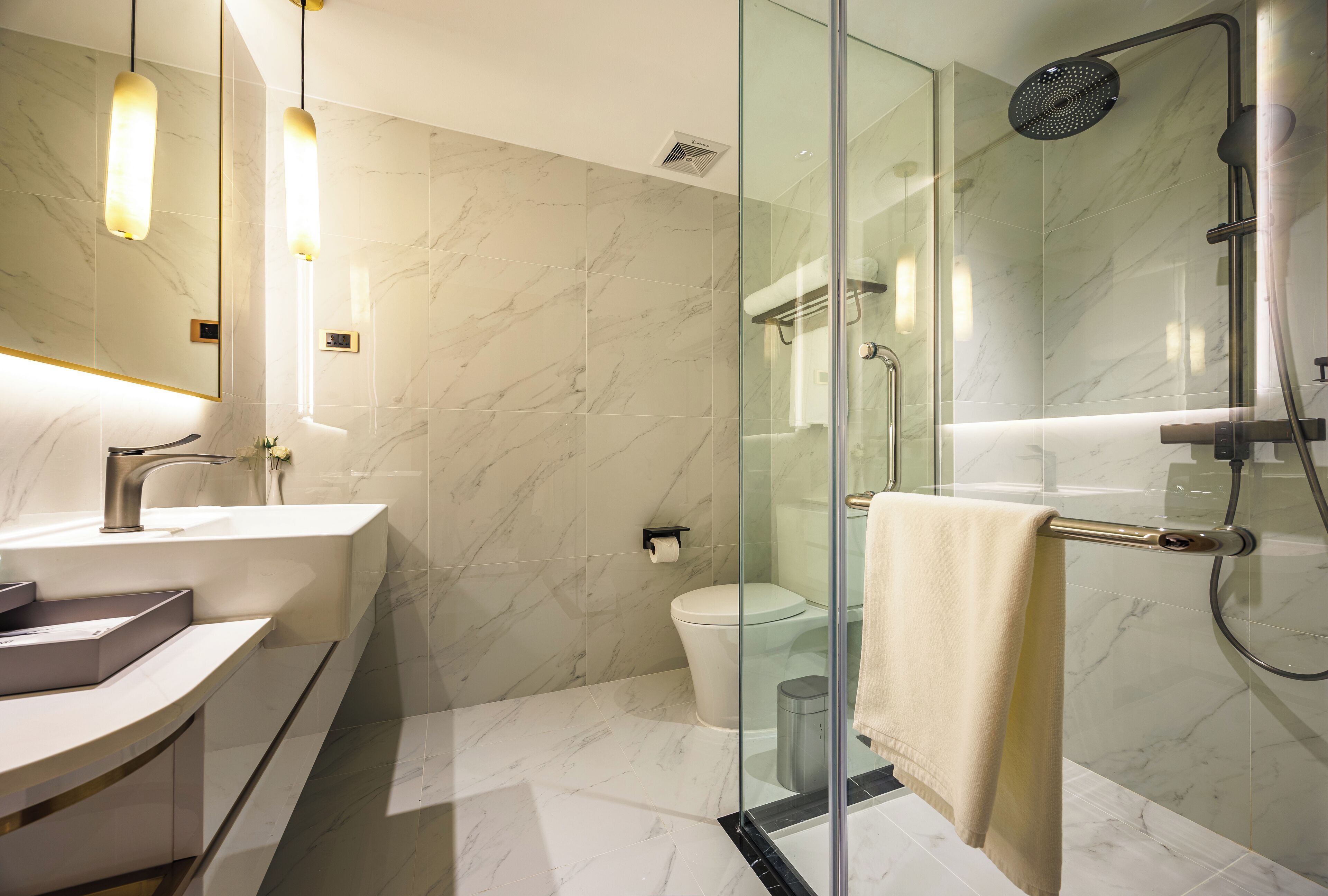 A modern bathroom with a glass shower enclosure, a white sink, and a marble-tiled wall.