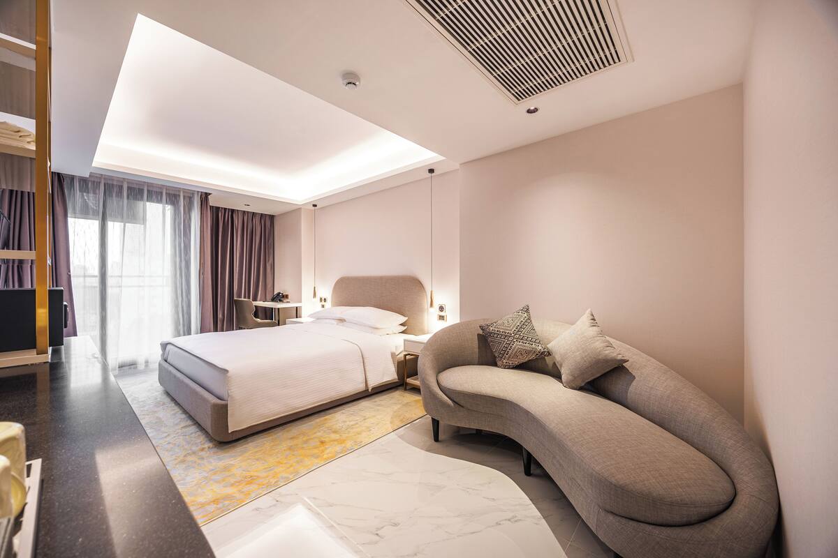 Une chambre d’hôtel moderne avec un canapé incurvé, un grand lit et un dressing.