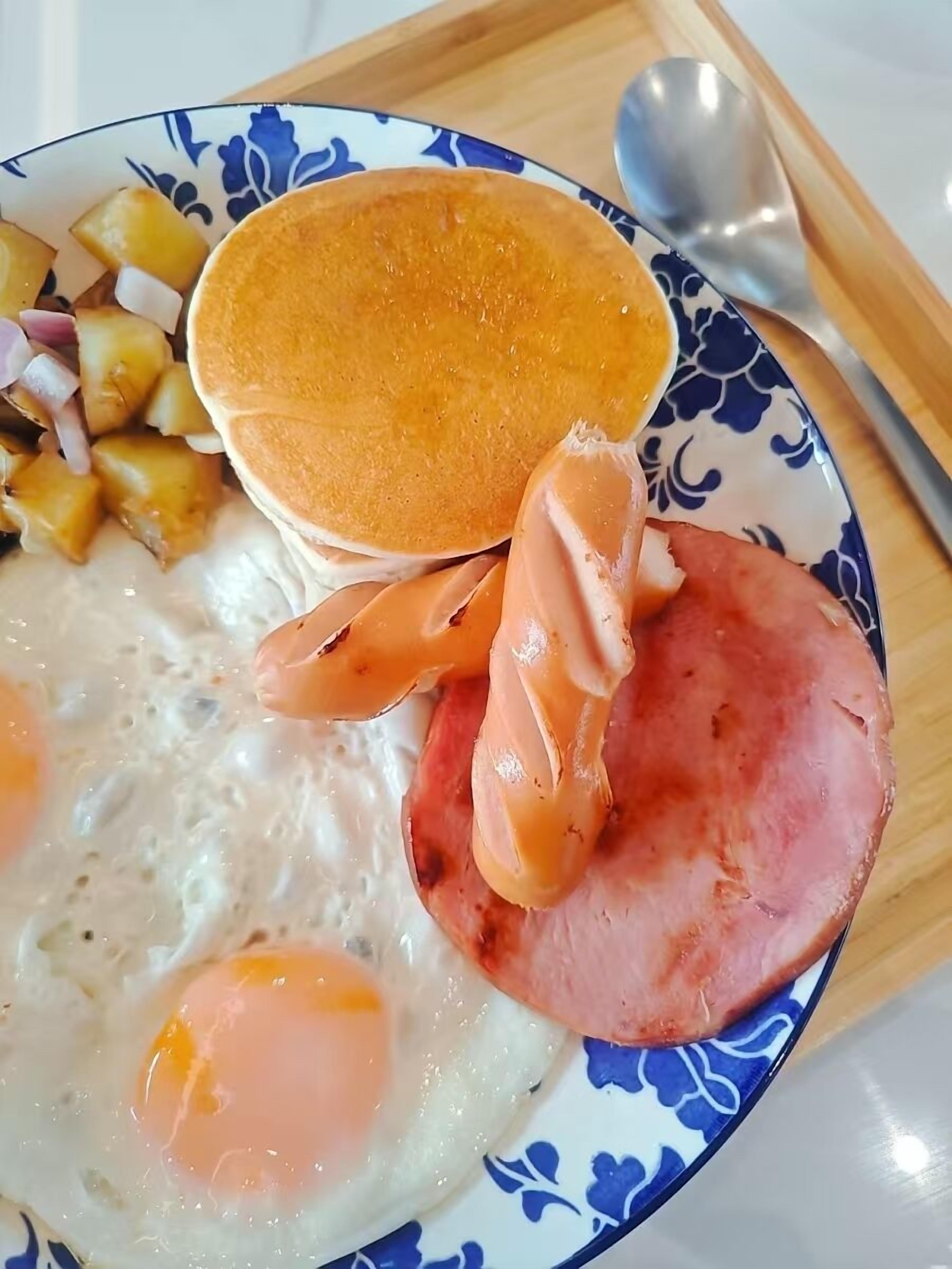 A plate with pancakes, ham, eggs, and potatoes.