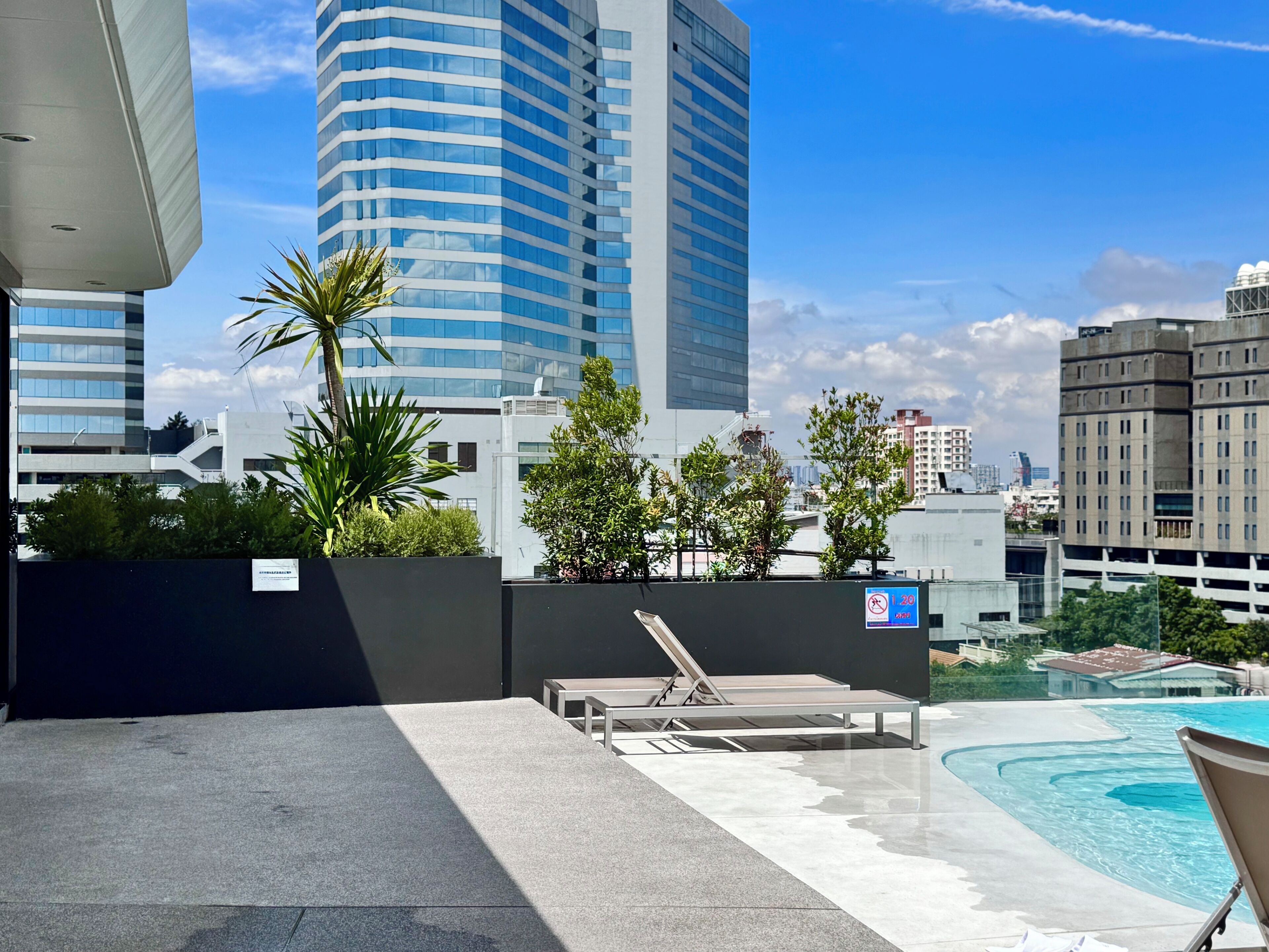 Un área de piscina en la azotea con sillones de descanso, una fuente de agua y vistas de edificios circundantes.