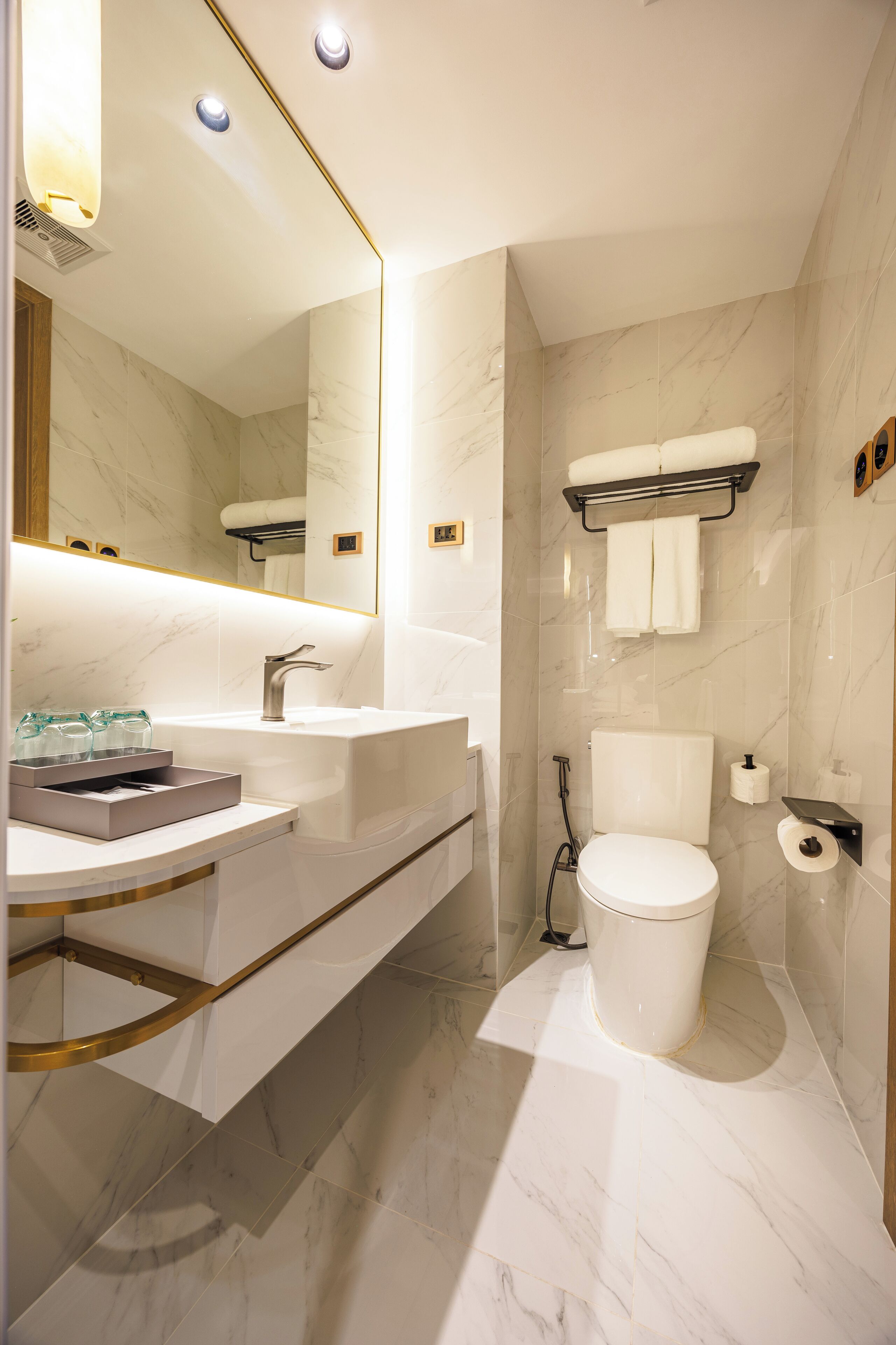 A modern bathroom with a marble floor, a large mirror, a white sink, and a toilet.