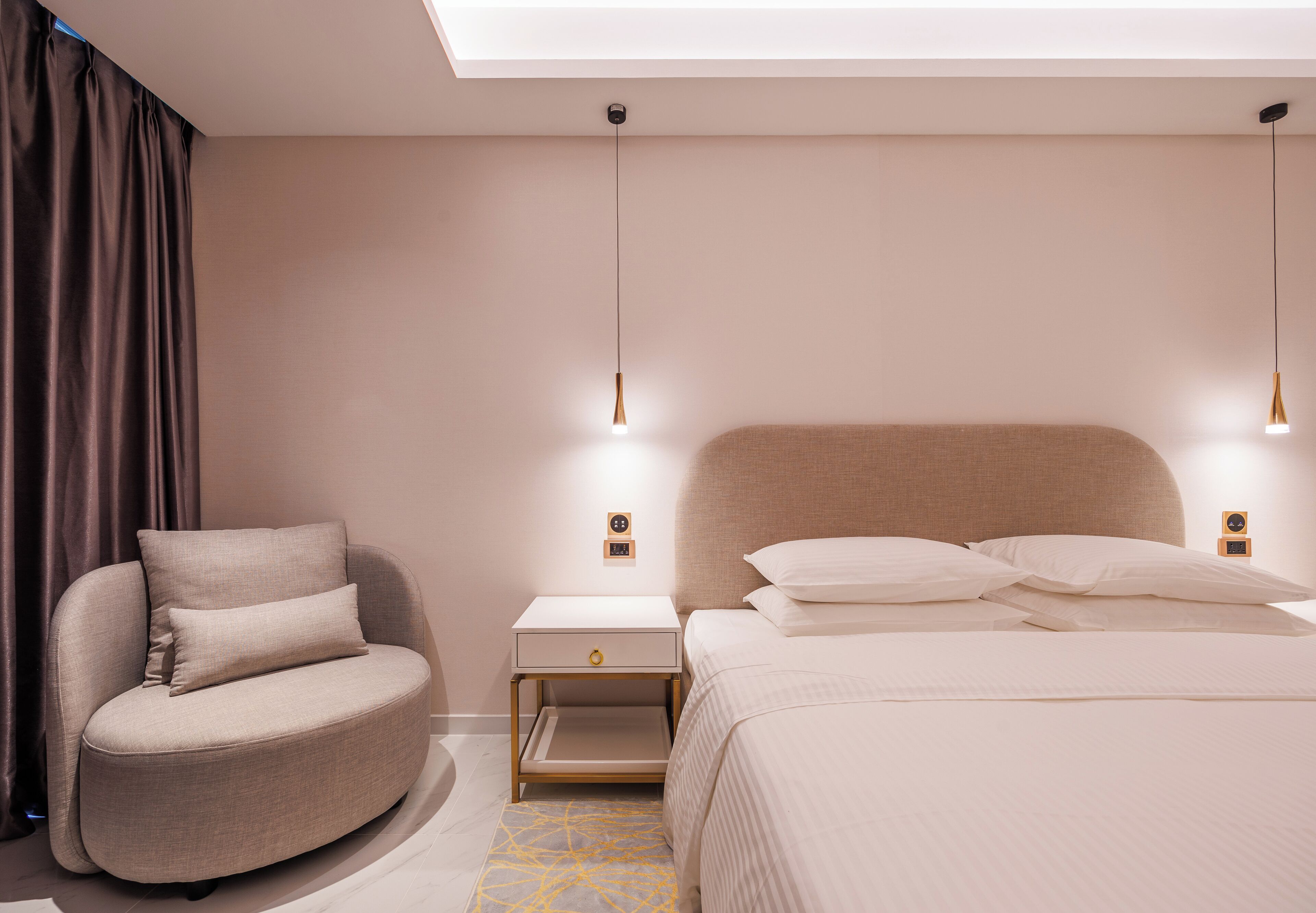Un dormitorio moderno con un sofá curvo, una cama con muchos almohadones, lámparas de noche y una mesita de noche con cajón.