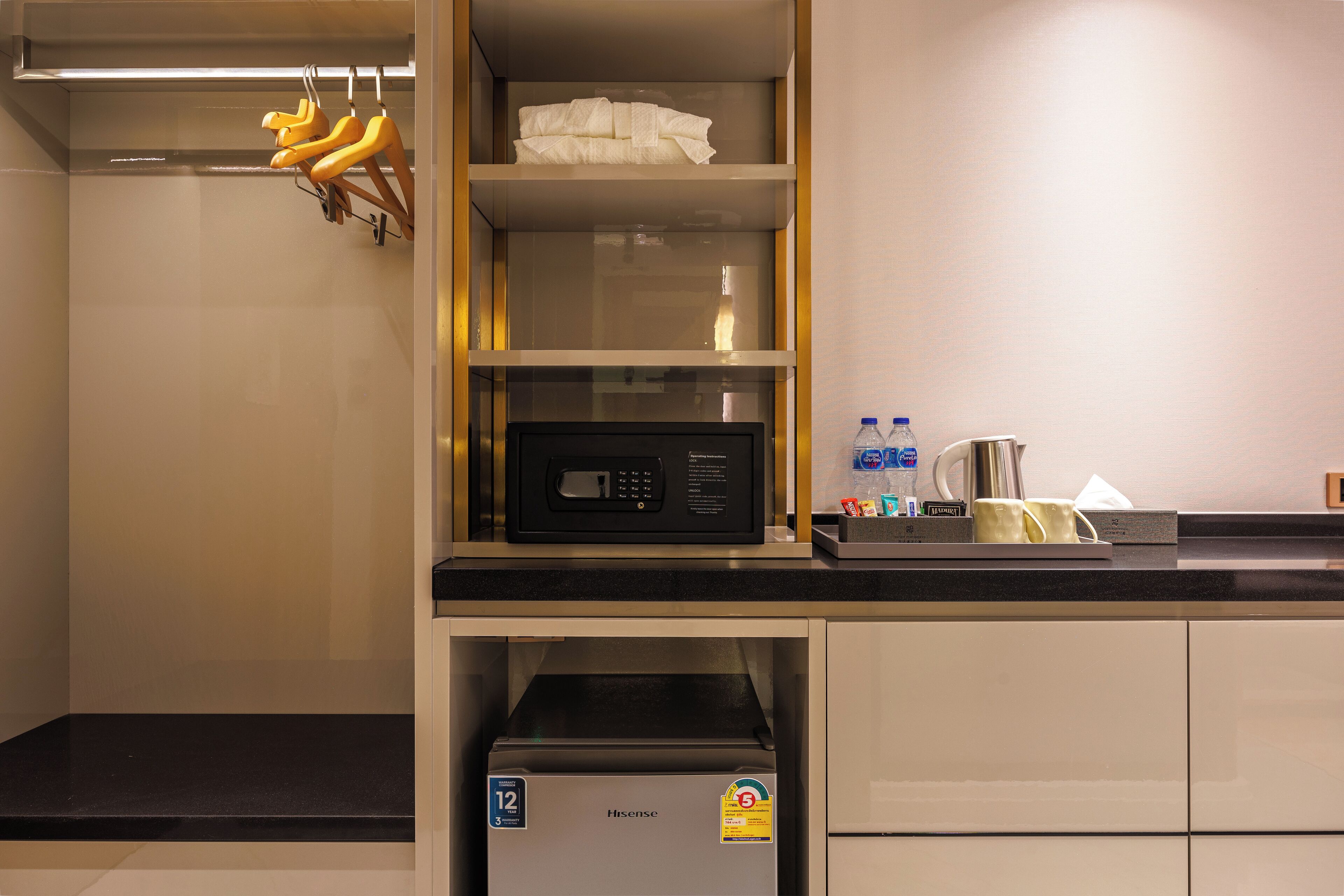 A compact kitchenette with a microwave, a small refrigerator, and a shelf with a bottle and a cup.