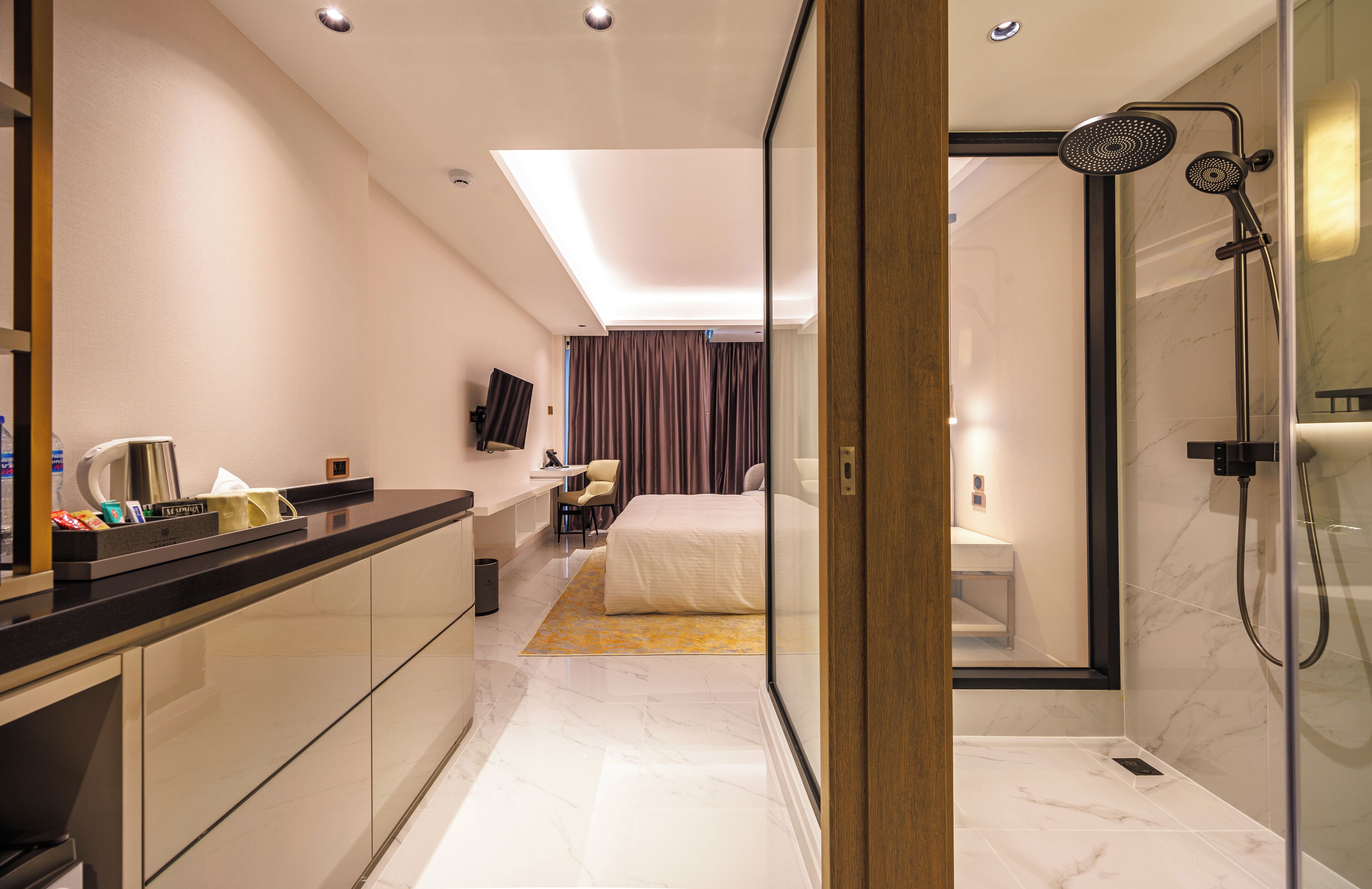 A modern hotel room with a large bed, a desk with a chair, a shower area, and a TV mounted on the wall.