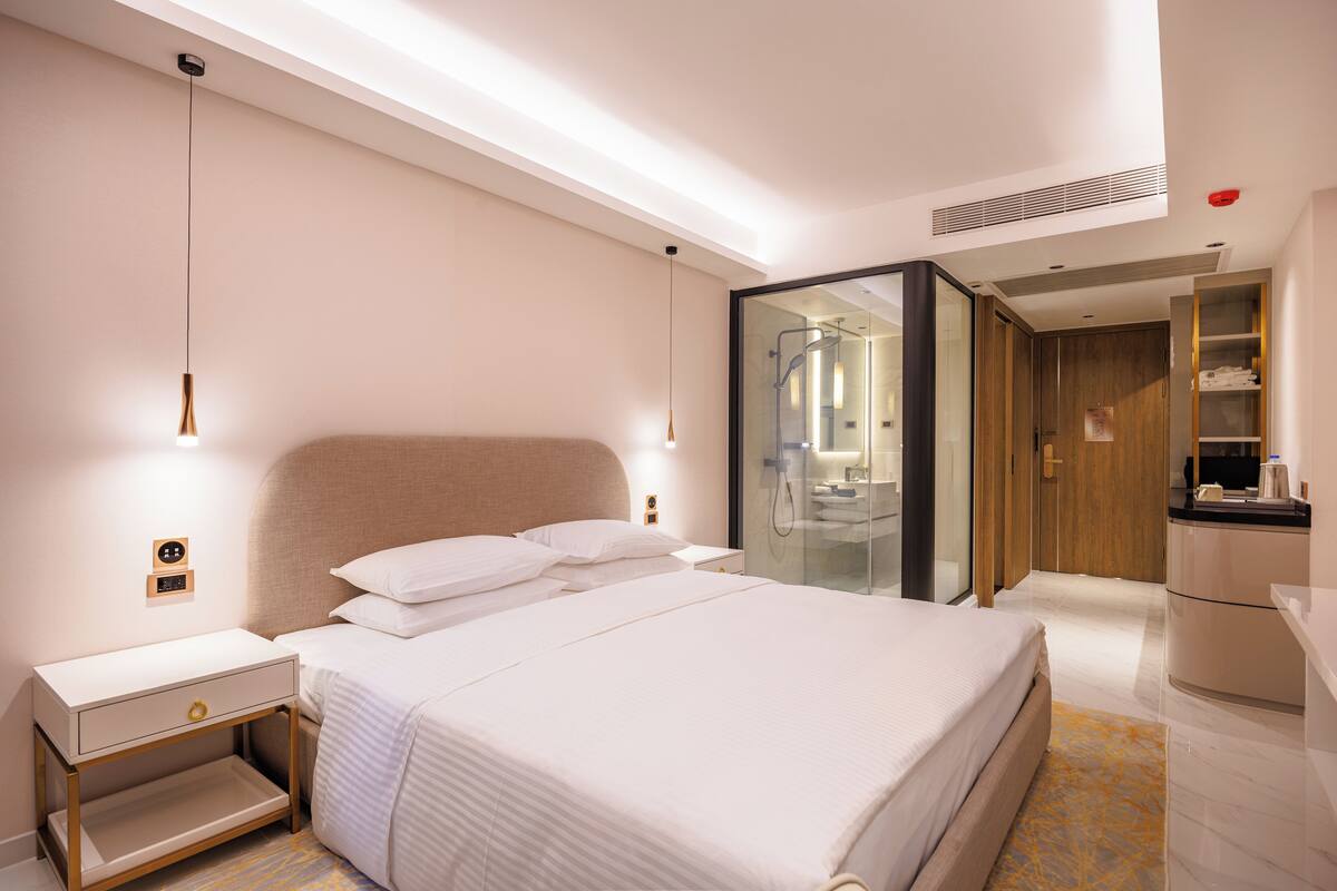 Une chambre d’hôtel moderne dotée d’un grand lit, de tables de chevet, d’une armoire intégrée et d’une cabine de douche en verre.