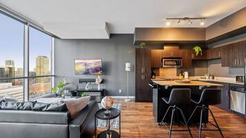 A modern apartment with a living room, kitchen, and large windows overlooking a cityscape.