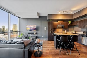 A modern apartment with a living room, kitchen, and large windows overlooking a cityscape. - King Bed | Calgary Tower Views |Walk to Saddledome (Calgary)