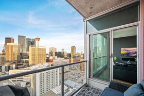 A balcony with a city view, a sliding glass door, a television, and a small table with decorative items. - King Bed | Calgary Tower Views |Walk to Saddledome (Calgary)
