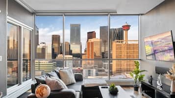 A modern living room with a city view, large windows, a sofa, a coffee table, and a TV.