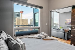 A modern hotel room with a large window, a bed, a seating area, and a view of a cityscape. - King Bed | Calgary Tower Views |Walk to Saddledome (Calgary)