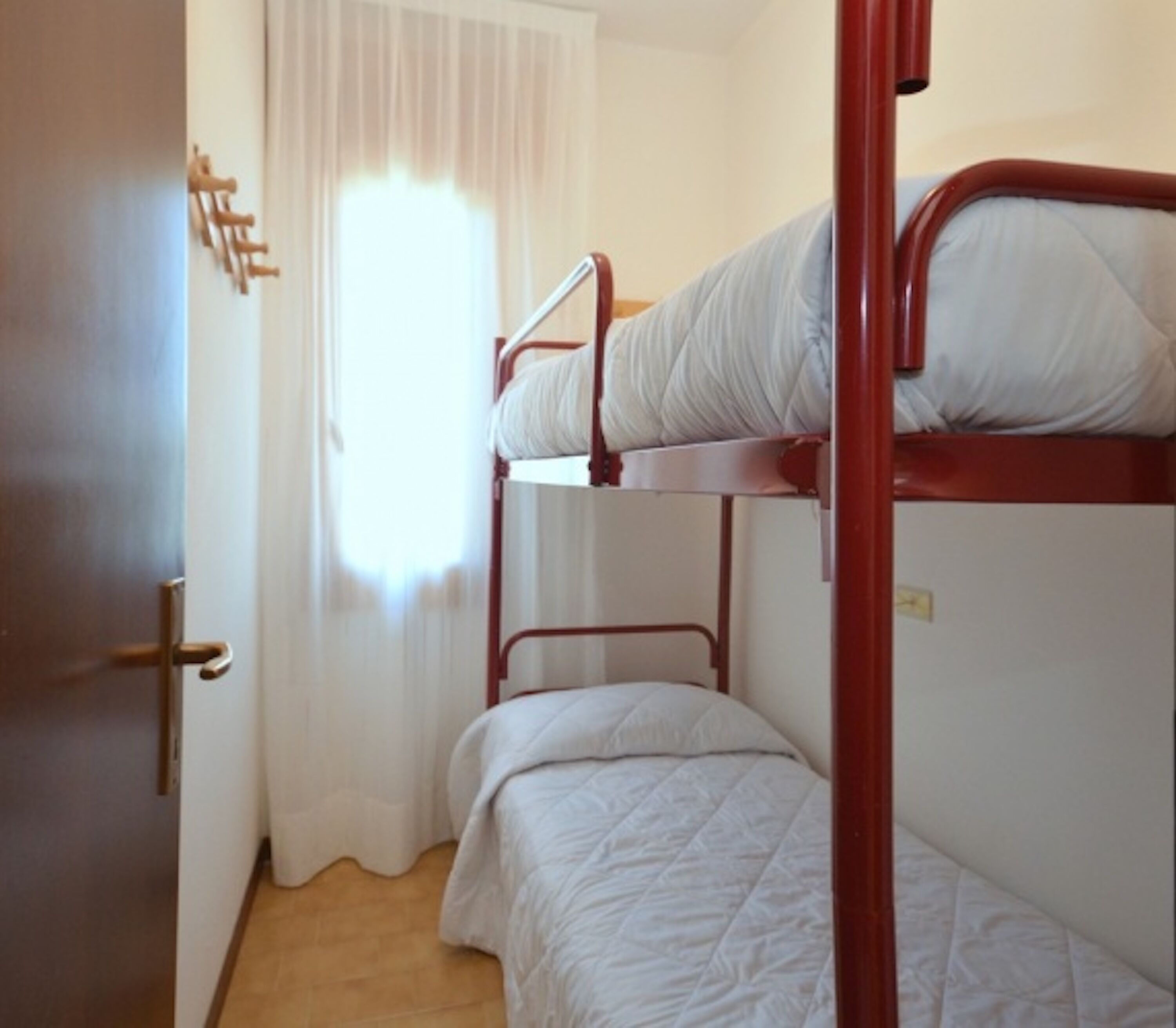 A bunk bed room with a wooden door and a window with white curtains.