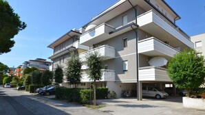 A multi-story residential building with balconies, a parking area, and a clear sky. - Cozy apartment with city views (Bibione)