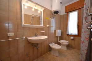 A bathroom with a sink, bidet, toilet, and a mirror with lights.