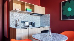 Una cocina compacta con encimera de granito, cafetera y tostadora. Hay dos sillas naranjas y una pequeña mesa redonda.