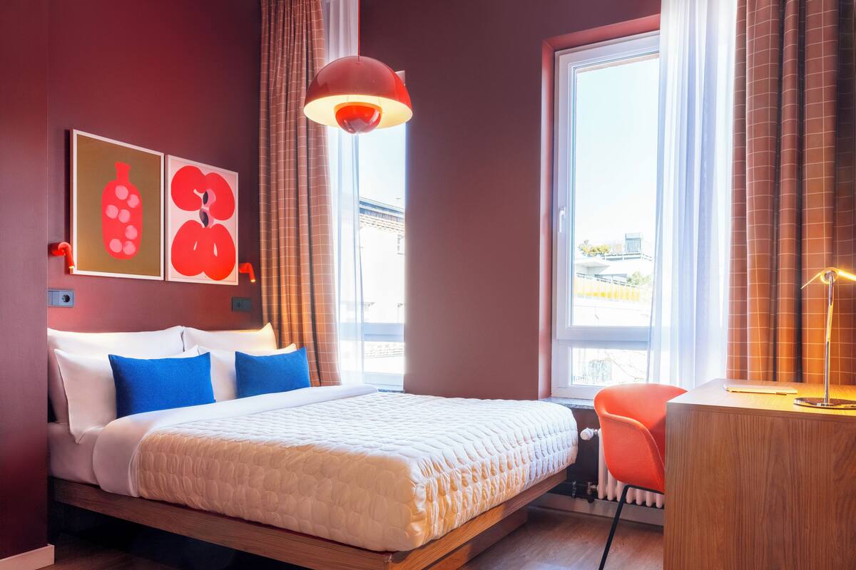 Una habitación de hotel moderna con una cama grande, un escritorio y una ventana con cortinas.
